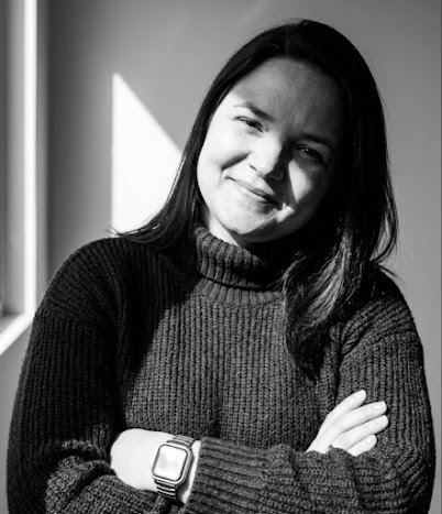 Lorena, de blusa de tricô e braços cruzados, sorrindo para a câmera